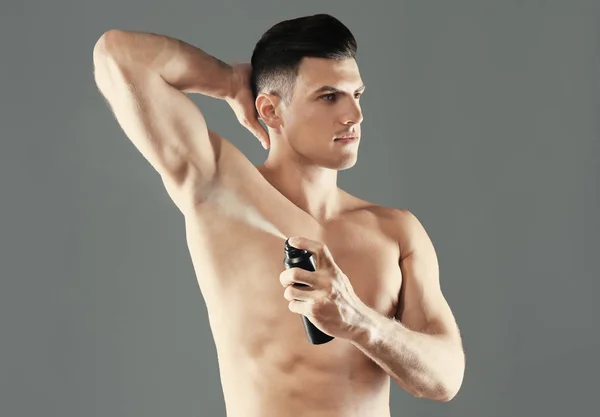Knappe jongeman met deodorant op grijze achtergrond — Stockfoto