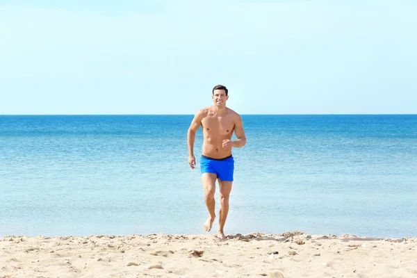 Bello giovane uomo che corre sulla spiaggia del mare — Foto Stock