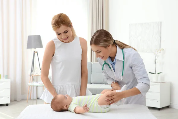 Ibu muda berdiri di dekat sofa sementara dokter memeriksa bayi di rumah — Stok Foto