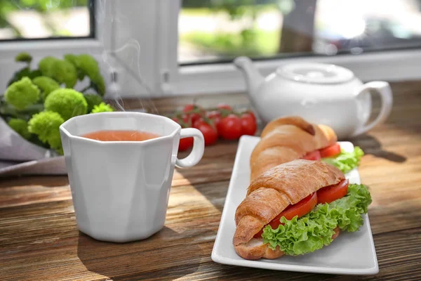 Sabrosos sándwiches de croissant y taza de té en el alféizar de la ventana —  Fotos de Stock