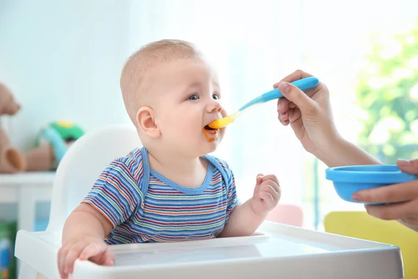 Mother feeding baby with spoon indoors — Stock Photo, Image