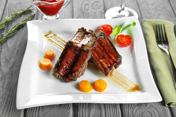 Placa con deliciosas costillas en mesa de madera — Foto de Stock