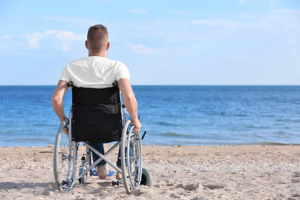 Deniz kıyısında tekerlekli sandalyede yaşlı bir adam.