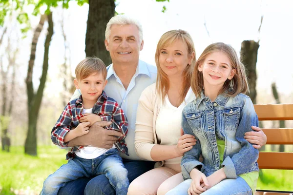 Niedliche glückliche Kinder mit Großeltern sitzen auf Bank im Frühlingspark — Stockfoto