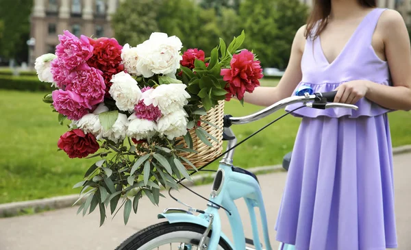 Leende flicka med cykel och korg med pioner på gatan — Stockfoto