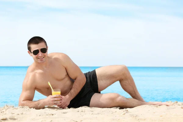 Pohledný mladý muž s nápoji na pláži moře — Stock fotografie