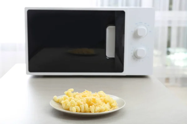 Тарелка с макаронами и сыром рядом с микроволновой печью — стоковое фото
