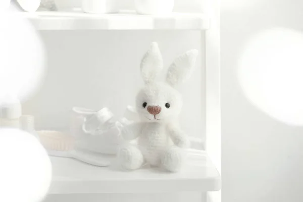 Schattig gebreid speelgoed bunny en baby accessoires op plank in lichte kamer — Stockfoto