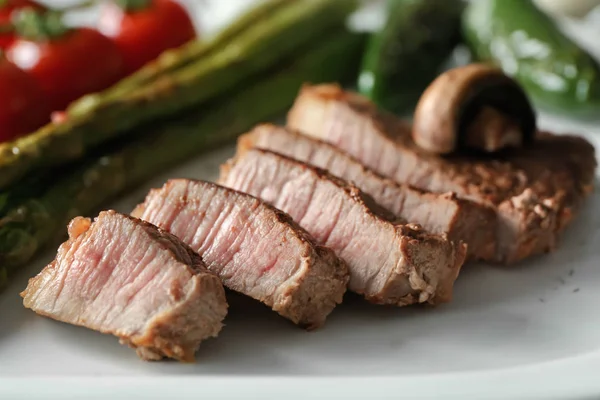 Sliced steak with vegetables on white plate, closeup — Stock Photo, Image