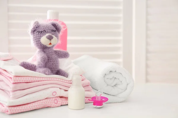 Knitted toy bear, baby clothes and accessories on table in room — Stock Photo, Image