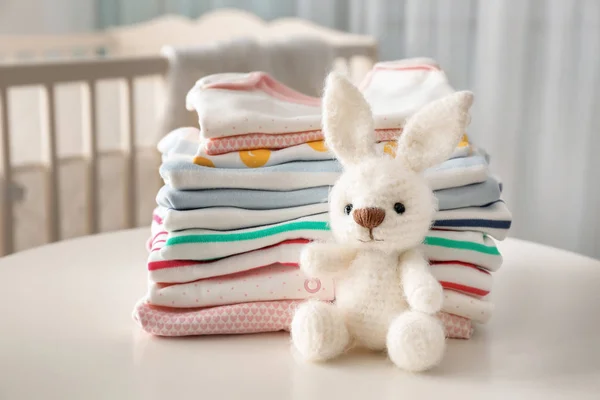 Conejito de juguete de punto y ropa de bebé en la mesa —  Fotos de Stock