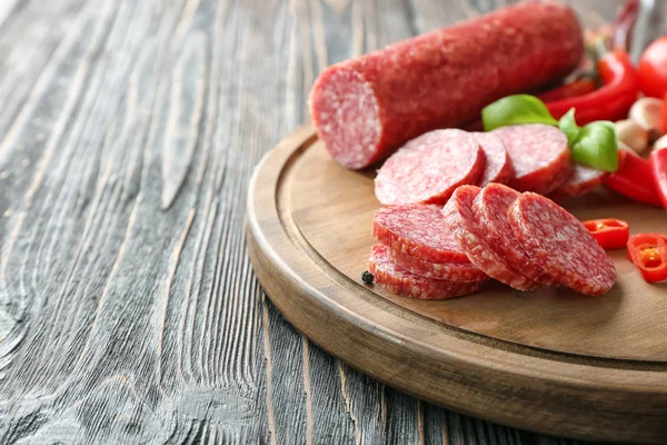 Tablero de madera con deliciosa salchicha en rodajas y chile en la mesa — Foto de Stock