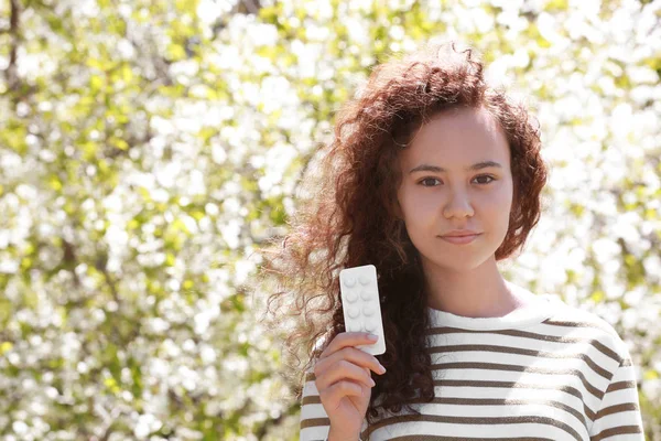 Концепция аллергии. Молодая девушка держит таблетки среди цветущих деревьев в парке — стоковое фото