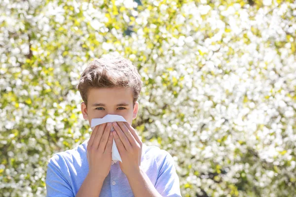 Allergiekonzept. Niesender kleiner Junge mit Nasenwischer zwischen blühenden Bäumen im Park — Stockfoto