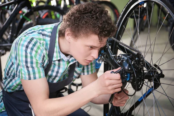 Joven comprobando bicicleta en taller de reparación — Foto de Stock