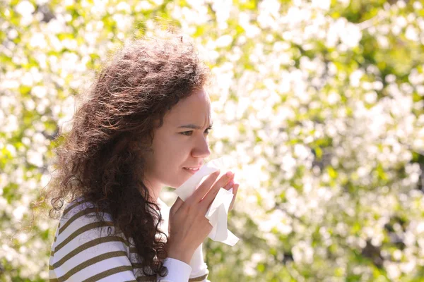 Alergie koncept. Kýchací mladá dívka s hladící nos mezi kvetoucí stromy v parku — Stock fotografie