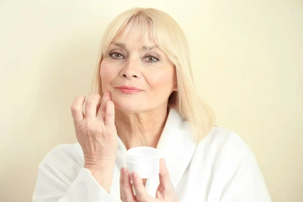 Starší Žena Použitím Krém Obličej Proti Světlé Pozadí — Stock fotografie
