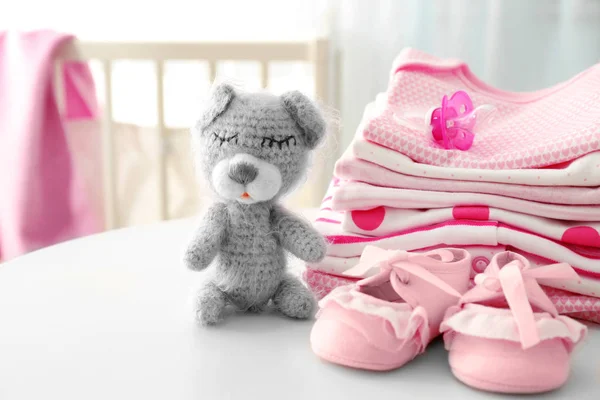 Urso de brinquedo de malha e roupas de bebê na mesa — Fotografia de Stock