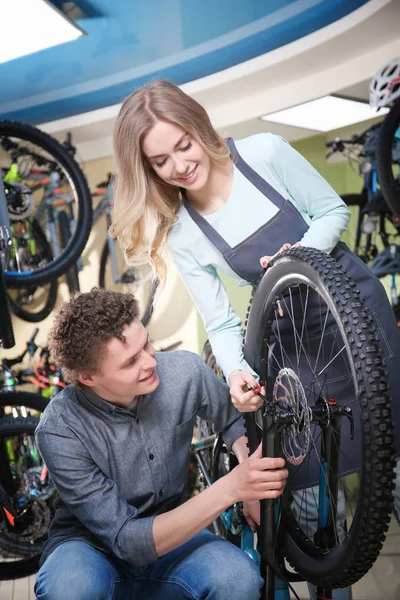 Junger Mann und hübsche Frau kontrollieren Fahrrad in Werkstatt — Stockfoto