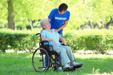 Tekerlekli sandalye ile genç erkek gönüllü açık havada üzerinde mutlu kadın kıdemli