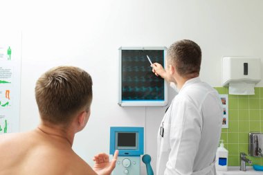 Orthopedist showing x-ray image to patient in clinic clipart