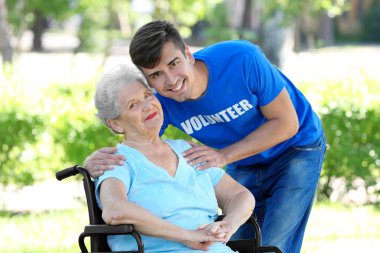 Tekerlekli sandalye ile genç erkek gönüllü açık havada üzerinde mutlu kadın kıdemli