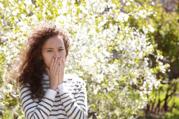 Allergy concept. Young woman suffering from cough among blooming trees in park — Stock Photo, Image