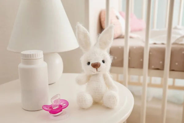 Brinquedo de bebê, chupeta e talco corporal na mesa na sala de luz — Fotografia de Stock