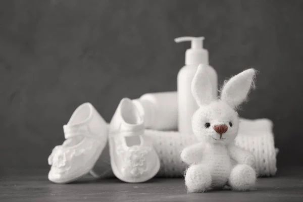 Cute knitted toy bunny and baby accessories on gray background — Stock Photo, Image