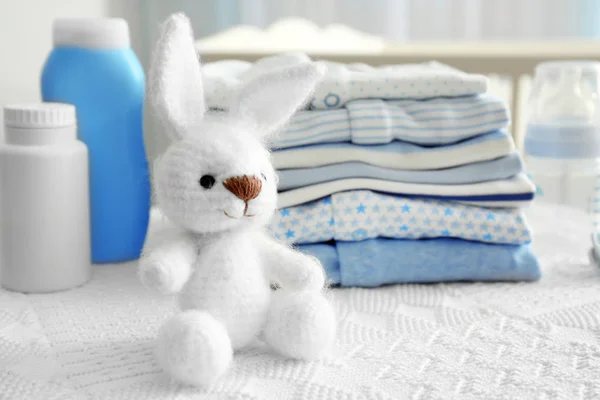 Knitted toy bunny and baby clothes on table