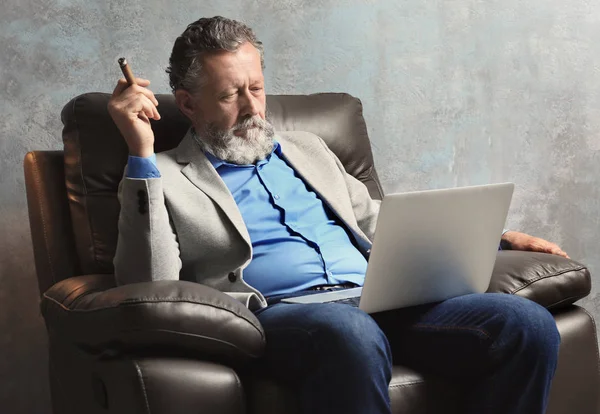 Hombre mayor guapo sentado en sillón con portátil — Foto de Stock