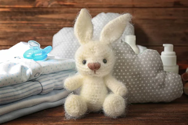 Cute knitted toy bunny and baby accessories on wooden background — Stock Photo, Image