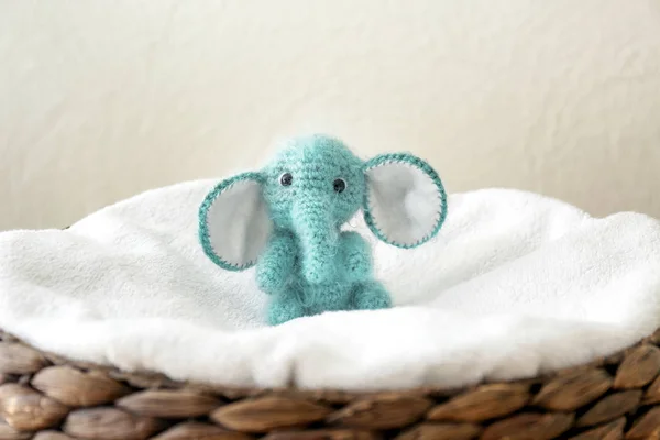 Cute knitted toy elephant in wicker basket on light background — Stock Photo, Image