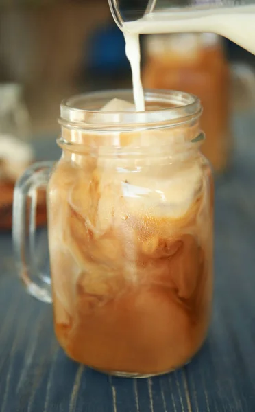 Pouring milk into mason jar with cold brew coffee on wooden table — Stock Photo, Image