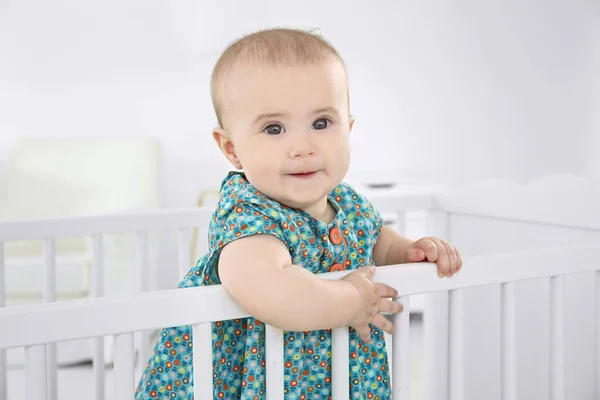 Cute little girl standing in crib at home — Stock Photo, Image