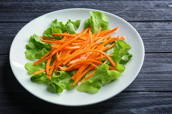 Teller mit leckerem Karottensalat auf Holztisch — Stockfoto