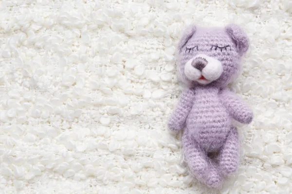 Cute knitted bear on white fluffy fabric background