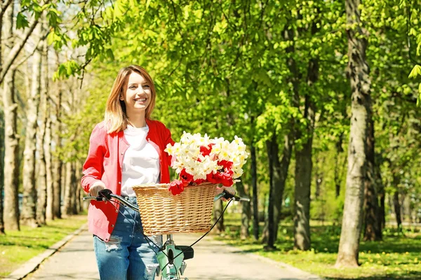 Ung flicka med cykel och korg med blommor — Stockfoto