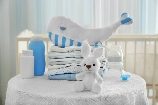 Knitted toy bunny, baby clothes and accessories on table in room — Stock Photo, Image