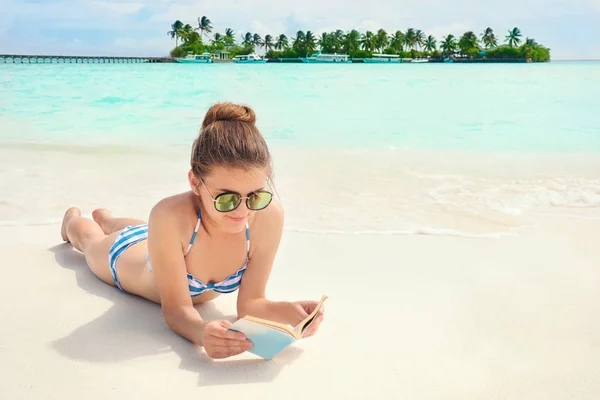 Hermosa joven leyendo libro mientras se encuentra en la playa del mar — Foto de Stock