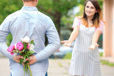 Genç adam arkasına park kız arkadaşı için güzel çiçekler buket gizleme