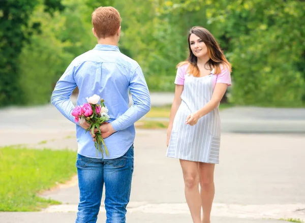 Giovane uomo nascondendo bouquet di bei fiori per la sua ragazza dietro la schiena nel parco — Foto Stock