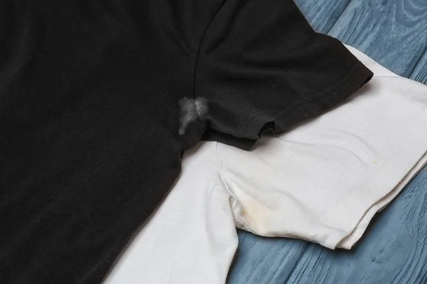 Black and white t-shirts with stains of sweat and deodorant on wooden background. Concept of hygiene