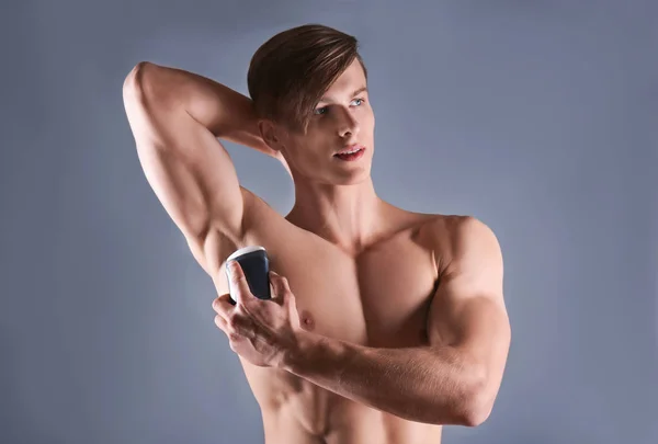 Pohledný mladý muž s deodorant na šedém pozadí — Stock fotografie