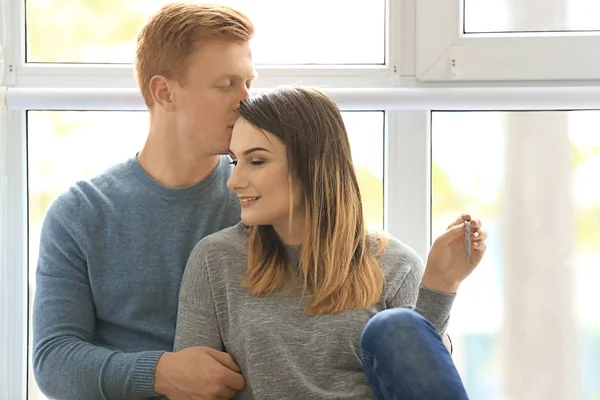 Schönes Paar sitzt am Fenster mit Schlüsseln aus neuer Wohnung — Stockfoto