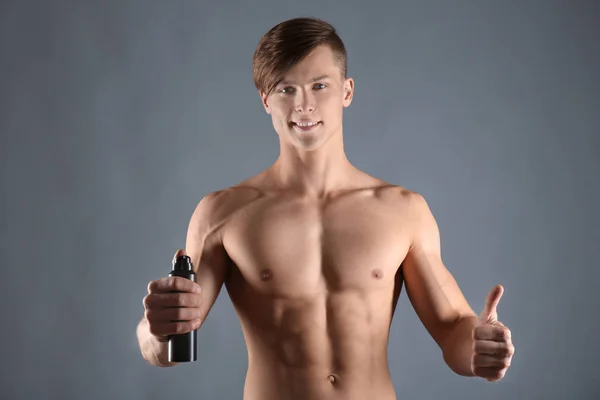 Joven guapo con desodorante sobre fondo gris — Foto de Stock