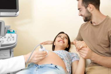 Young pregnant couple undergoing ultrasound scan in clinic clipart