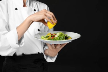 Koyu arka plan üzerine limon suyu ile genç kadın Şef giyinme salatası