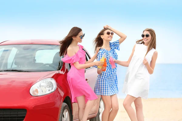 Belle giovani donne con bevande alcoliche vicino alla macchina in località balneare — Foto Stock
