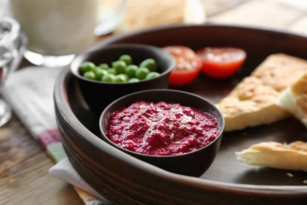 Bowl with delicious beet hummus, peas, tomato and bread on table — Stock Photo, Image